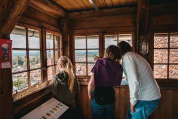 Drei Personen schauen vom Schloss hinunter auf die Stadt Burgdorf. Sie zeigen, was sie dort sehen.